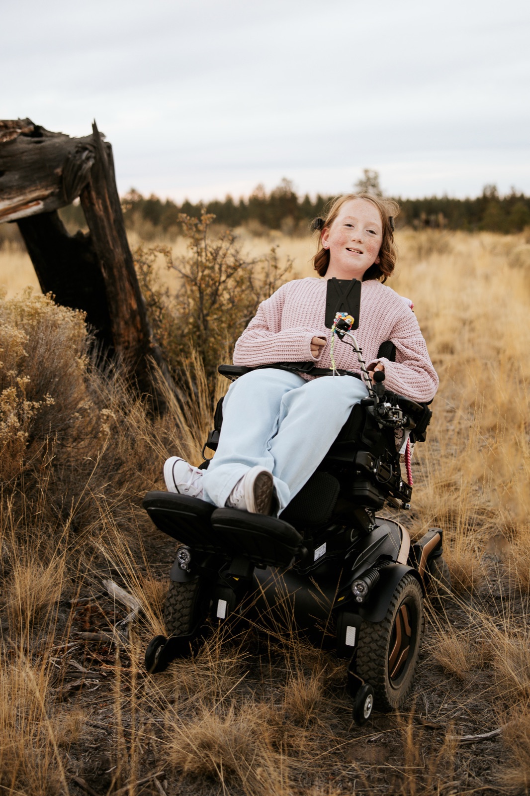 Bella, a bright, smiling girl with freckles, in her wheelchair in the high desert